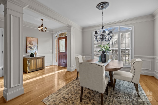 dining area with light wood-type flooring, ornate columns, crown molding, and an inviting chandelier