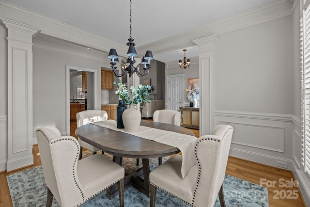 dining area with decorative columns, ornamental molding, light wood-type flooring, and an inviting chandelier