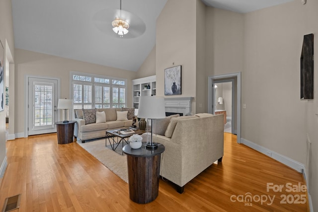 living room with ceiling fan, a high ceiling, and light wood-type flooring