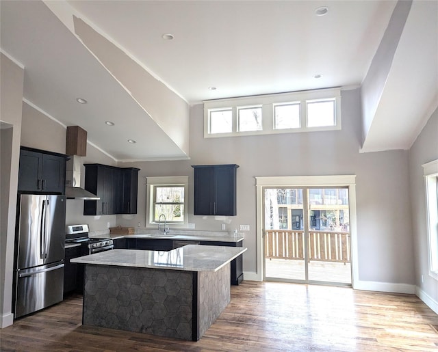 kitchen with light stone counters, wood finished floors, a kitchen island, ornamental molding, and appliances with stainless steel finishes