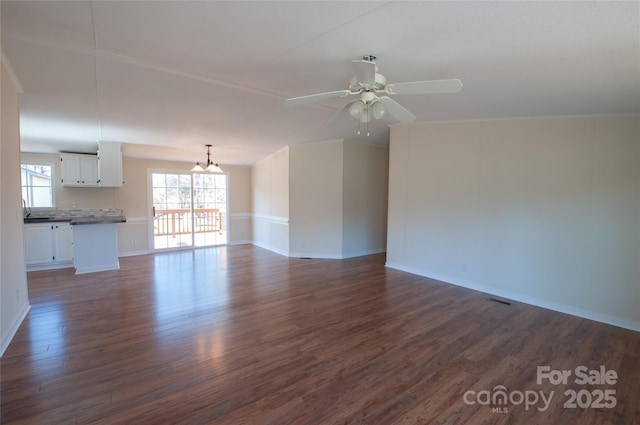 unfurnished living room with ceiling fan with notable chandelier and dark hardwood / wood-style floors