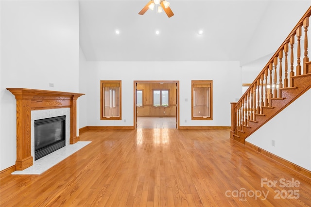 unfurnished living room with ceiling fan, light wood-type flooring, a high end fireplace, and a towering ceiling