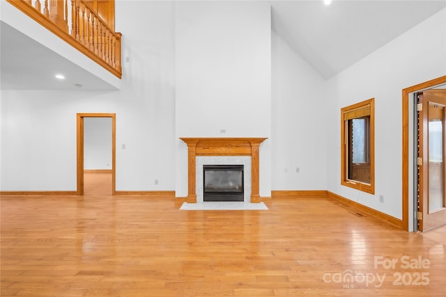 unfurnished living room featuring a premium fireplace, high vaulted ceiling, and light hardwood / wood-style floors