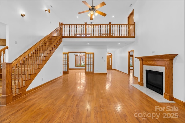 unfurnished living room with light wood-type flooring, a towering ceiling, ceiling fan, a fireplace, and french doors