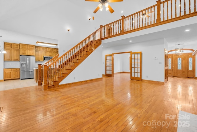 unfurnished living room featuring ceiling fan with notable chandelier, light hardwood / wood-style floors, french doors, and a towering ceiling