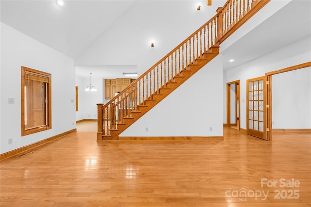 unfurnished living room with light hardwood / wood-style floors, high vaulted ceiling, and a chandelier