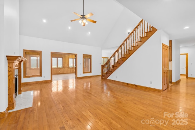 unfurnished living room with ceiling fan, light wood-type flooring, a premium fireplace, and a towering ceiling