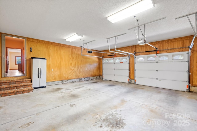 garage featuring white fridge, a garage door opener, and wood walls