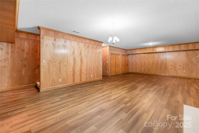 basement featuring wood walls, a notable chandelier, ornamental molding, wood-type flooring, and a textured ceiling