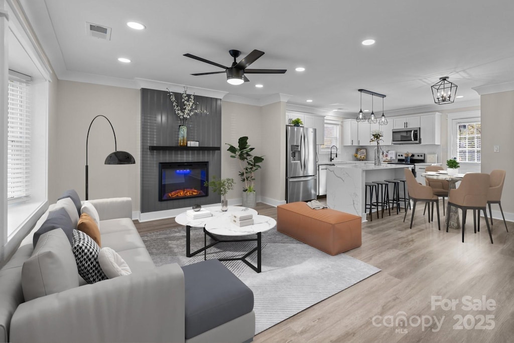 living room featuring ceiling fan with notable chandelier, sink, crown molding, light hardwood / wood-style flooring, and a fireplace