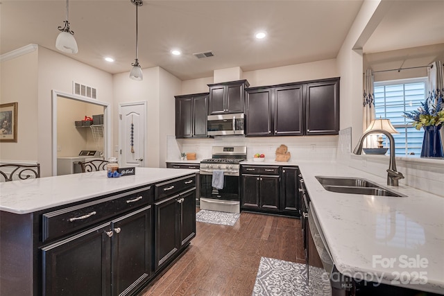 kitchen featuring washer and clothes dryer, a center island, sink, decorative light fixtures, and stainless steel appliances