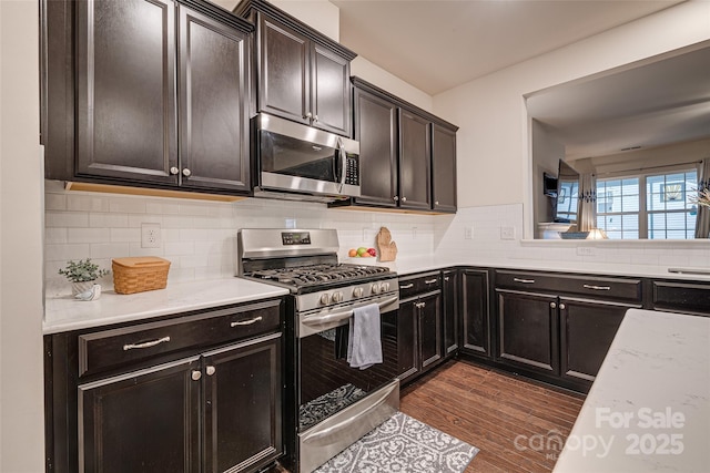 kitchen with appliances with stainless steel finishes, backsplash, light stone counters, and dark wood-type flooring