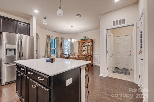 kitchen with dark wood-type flooring, a kitchen breakfast bar, stainless steel fridge with ice dispenser, decorative light fixtures, and a kitchen island