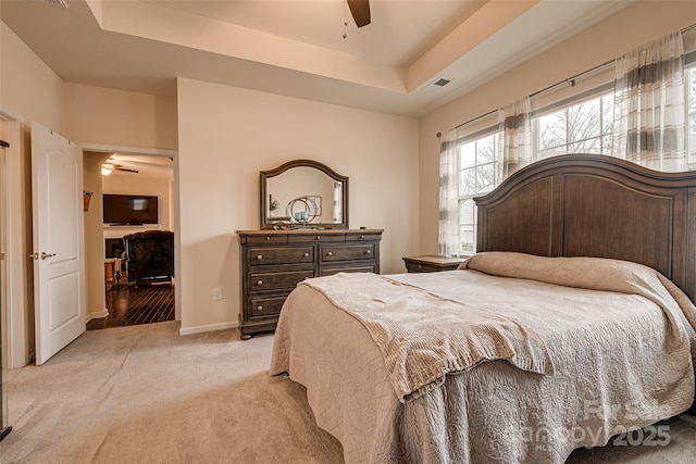 bedroom with ceiling fan, light colored carpet, and a tray ceiling