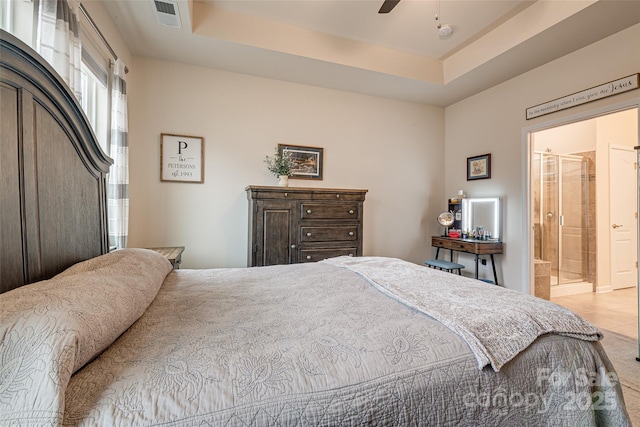 bedroom with a tray ceiling, ensuite bath, and ceiling fan