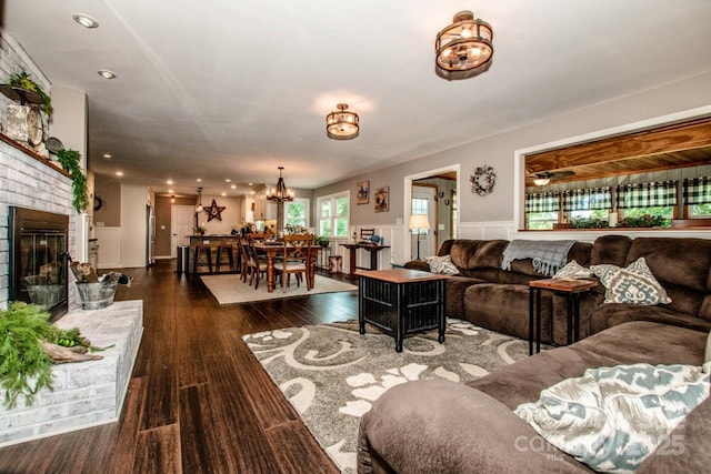 living room with ceiling fan with notable chandelier, dark wood-type flooring, and a brick fireplace