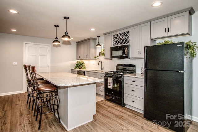 kitchen with light stone countertops, black appliances, light hardwood / wood-style flooring, a center island, and gray cabinets