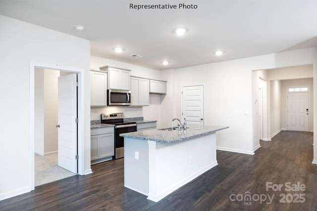 kitchen with a kitchen island with sink, sink, light stone countertops, appliances with stainless steel finishes, and dark hardwood / wood-style flooring