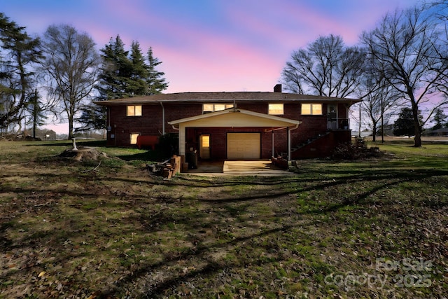 back house at dusk with a lawn and a garage