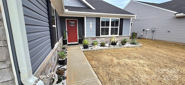 entrance to property featuring stone siding, roof with shingles, and a yard