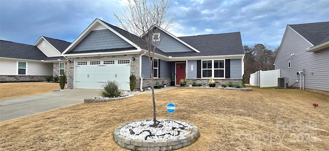 craftsman-style house featuring central air condition unit, a garage, stone siding, concrete driveway, and a front yard