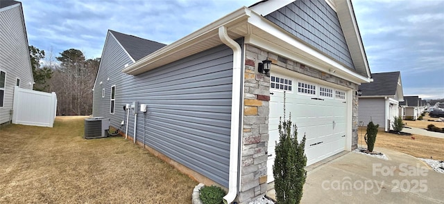 view of side of home featuring a garage, stone siding, fence, and central AC unit