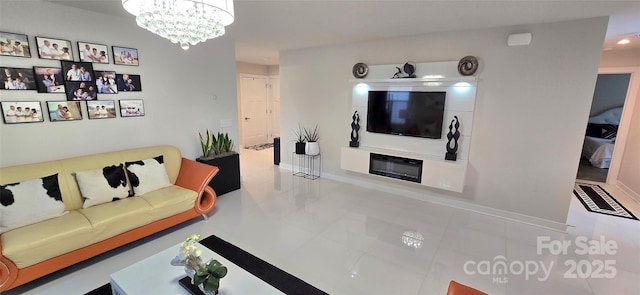 living area with a chandelier, a glass covered fireplace, and baseboards