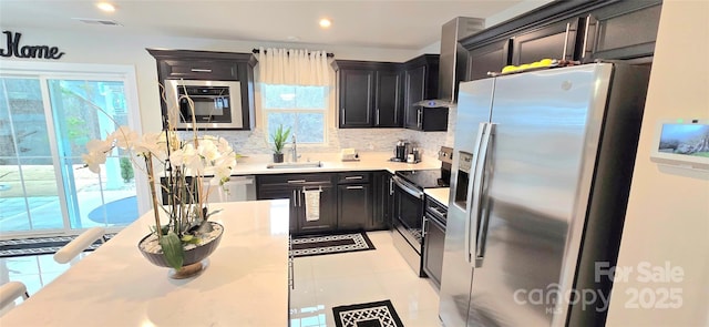 kitchen with sink, wall chimney range hood, backsplash, light tile patterned floors, and appliances with stainless steel finishes