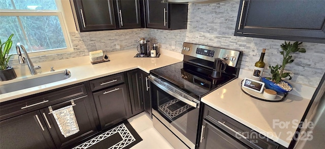 kitchen featuring stainless steel electric range, decorative backsplash, light countertops, and a sink