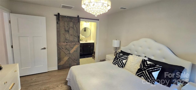 bedroom featuring a chandelier, a barn door, light hardwood / wood-style flooring, and ensuite bath