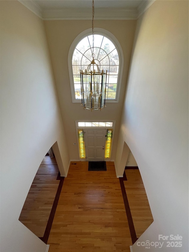 entrance foyer featuring ornamental molding, a towering ceiling, hardwood / wood-style flooring, and a notable chandelier