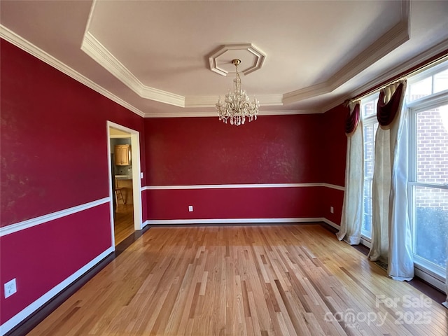 spare room with hardwood / wood-style floors, a raised ceiling, ornamental molding, and a notable chandelier