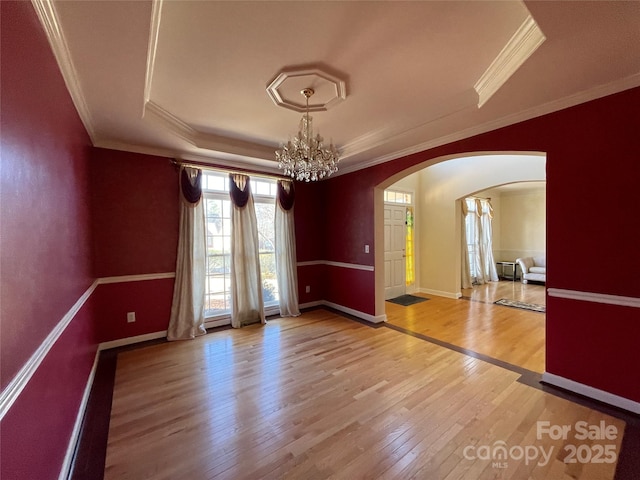 empty room with wood-type flooring, an inviting chandelier, a raised ceiling, and crown molding