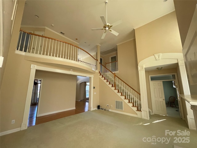 unfurnished living room with carpet flooring, a towering ceiling, ceiling fan, and crown molding