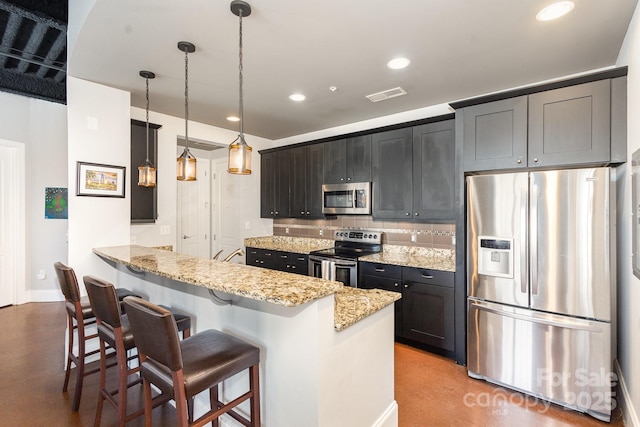 kitchen with hanging light fixtures, stainless steel appliances, light stone counters, kitchen peninsula, and a breakfast bar