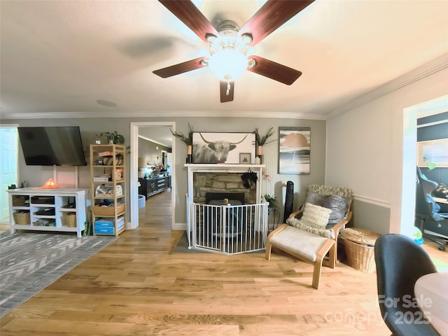 interior space featuring wood-type flooring, a stone fireplace, ceiling fan, and ornamental molding