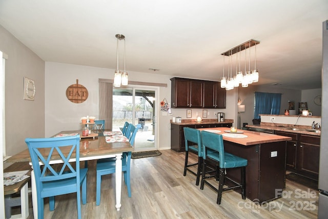 kitchen with dark brown cabinetry, a center island, light hardwood / wood-style flooring, pendant lighting, and a breakfast bar