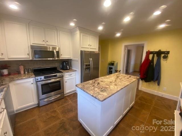 kitchen with stainless steel appliances, white cabinetry, a kitchen island, and light stone counters