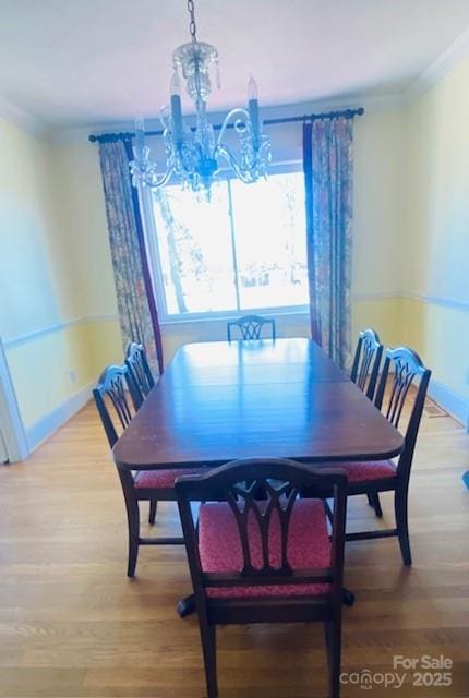 dining area with wood-type flooring, ornamental molding, and a notable chandelier