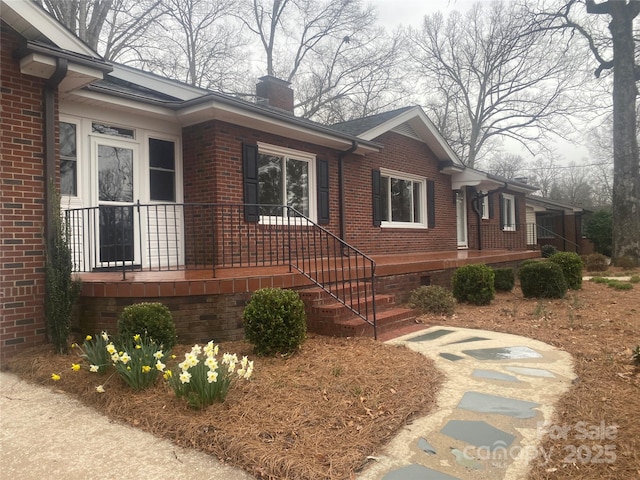 view of front of home featuring brick siding, covered porch, and a chimney