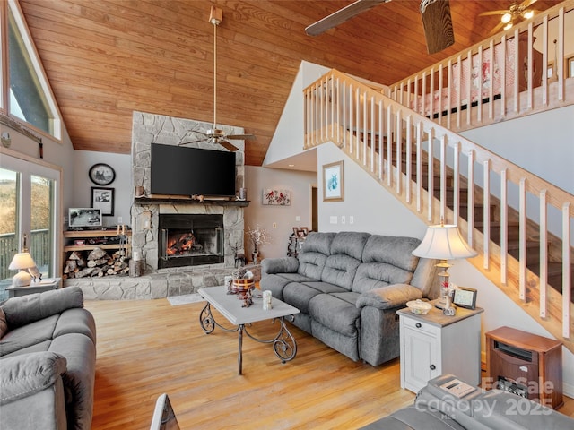 living room with high vaulted ceiling, a stone fireplace, ceiling fan, light hardwood / wood-style floors, and wood ceiling