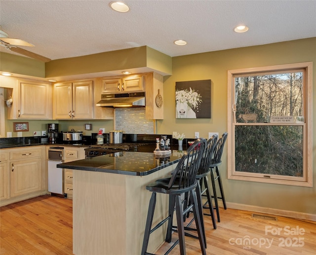 kitchen with kitchen peninsula, a kitchen breakfast bar, light hardwood / wood-style flooring, and dark stone countertops