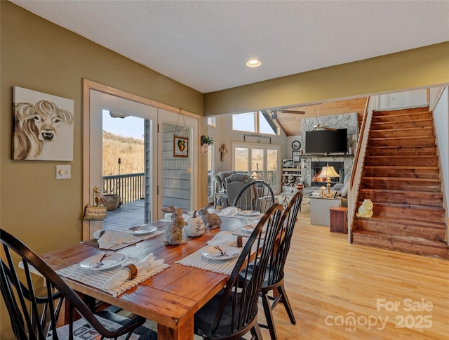 dining area with a stone fireplace, plenty of natural light, a textured ceiling, and light hardwood / wood-style flooring