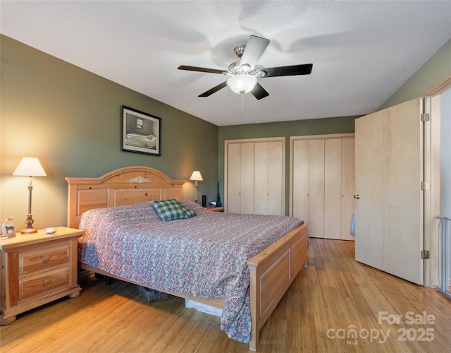 bedroom featuring a textured ceiling, ceiling fan, light hardwood / wood-style floors, and two closets