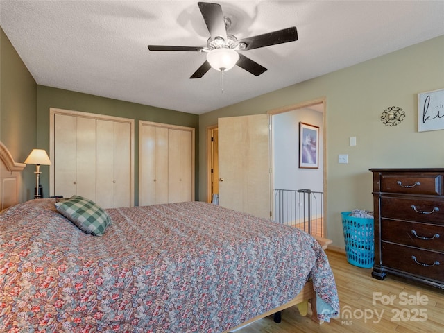 bedroom with a textured ceiling, ceiling fan, light hardwood / wood-style flooring, and multiple closets