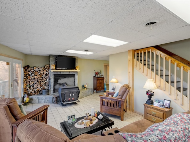 living room featuring a paneled ceiling, a wood stove, and light tile patterned floors