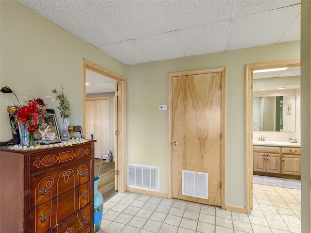 interior space with light tile patterned floors, a paneled ceiling, ensuite bath, and sink