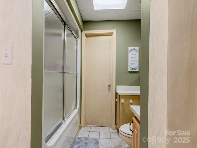 full bathroom featuring a drop ceiling, tile patterned flooring, toilet, shower / bath combination with glass door, and vanity