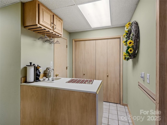 kitchen featuring light brown cabinetry, a drop ceiling, light tile patterned flooring, and sink