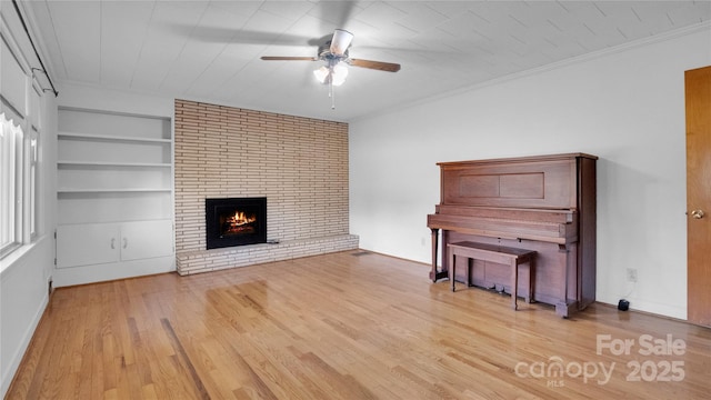 unfurnished living room featuring ornamental molding, ceiling fan, built in features, a fireplace, and hardwood / wood-style floors